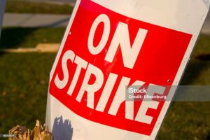 Discarded 'On Strike' placard in a trash bin after the strike ends, with a blurred background. Photographed in the warm glow of sunset light