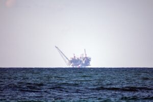 Offshore gas drilling platform at sea, visible against the horizon under a hazy sky.